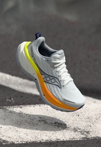 Sapatilha branca com um upper em malha e sola em degradê de amarelo a laranja. Apresenta detalhes em azul e um logótipo proeminente na lateral.