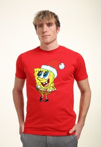Camiseta de algodón roja con un personaje de dibujos animados que lleva un gorro de Santa, con un esquema de colores amarillo y negro, diseño juguetón y mangas cortas.