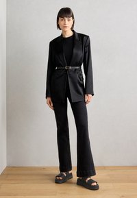 Svart skreddersydd blazer med innsnevret liv, sammen med svarte utsvingte jeans og kraftige svarte sandaler. Glatt stoff med minimalistisk design.