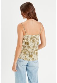 Camisole à motifs floraux en vert, beige et marron. Présente des bretelles fines et ajustables et une coupe ample. Associée à un jean taille haute bleu clair.