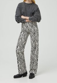 Pantalon imprimé zèbre noir et blanc à coupe droite et taille haute, associé à un sweat gris oversize et des bottines noires à talons épais.