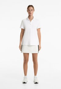 White polo shirt with a collar and button placket, paired with a light gray skirt featuring side slit details and black accents.