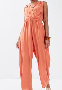 Combinaison orange décontractée avec un design croisé, sans manches et une taille froncée, présentant des jambes larges et amples. Texture de tissu lisse.
