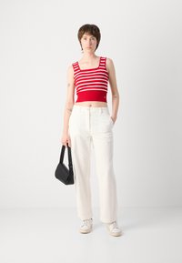 Débardeur rouge court avec rayures blanches, associé à un pantalon large blanc. Un sac à main noir et des baskets crème complètent la tenue.