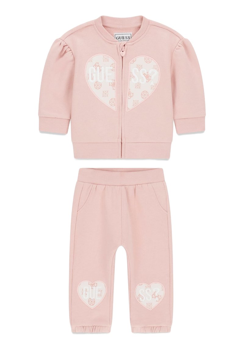 Lichtroze kindertrainingspak met een jas met rits, pofmouwen en een hartje, gecombineerd met bijpassende broek en ingestikte manchetten.