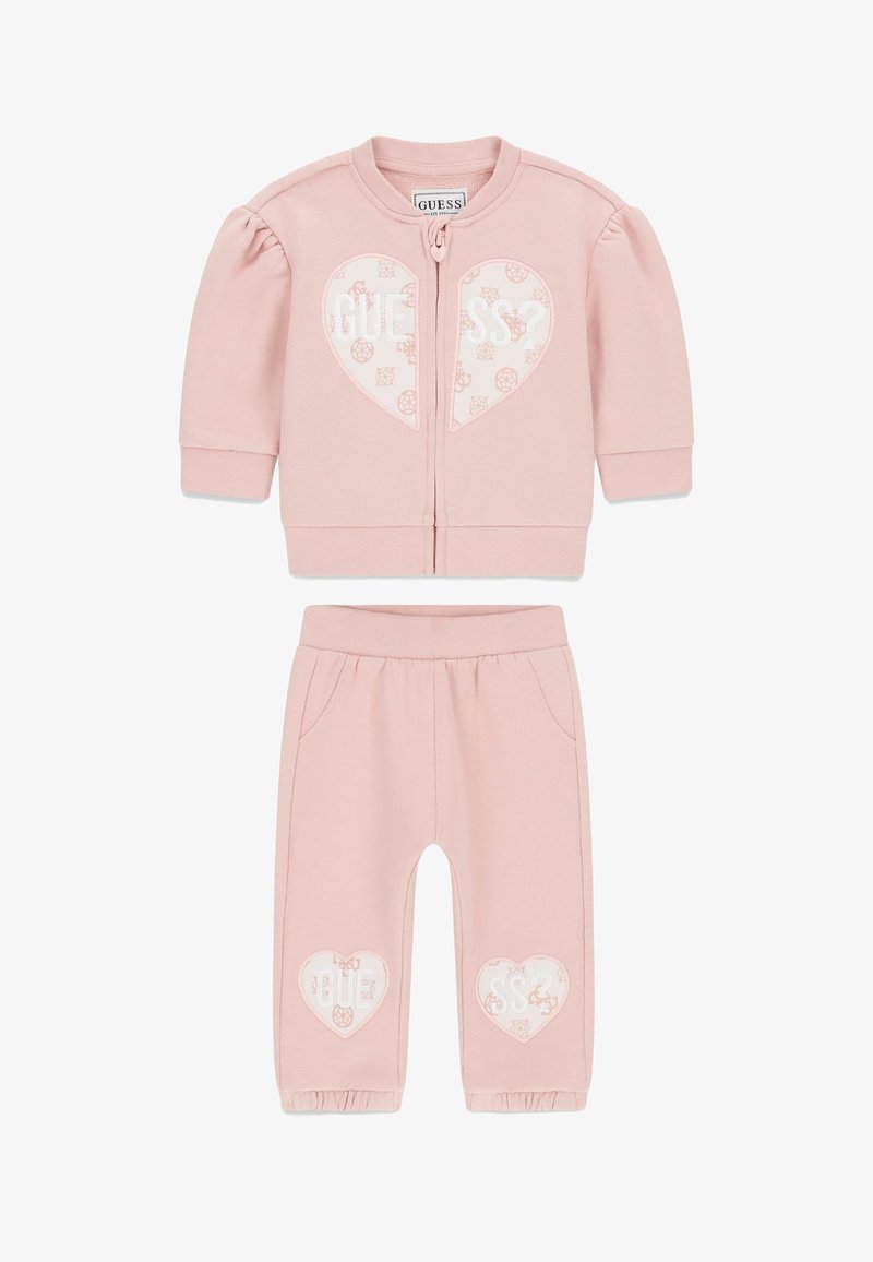 Lichtroze kindertrainingspak met een jas met rits, pofmouwen en een hartje, gecombineerd met bijpassende broek en ingestikte manchetten.