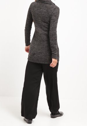 Maglione a maniche lunghe, grigio scuro, con un collo alto, tessuto con texture e silhouette aderente abbinato a pantaloni neri a vestibilità ampia.