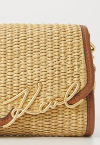 Woven straw handbag with brown leather accents, featuring a prominent gold "Karl" logo and a structured rectangular shape.