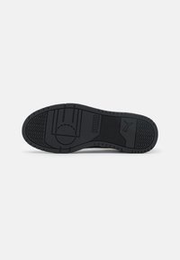 Black rubber sneaker sole featuring textured patterns, a central circle design, and prominent branding in raised letters.