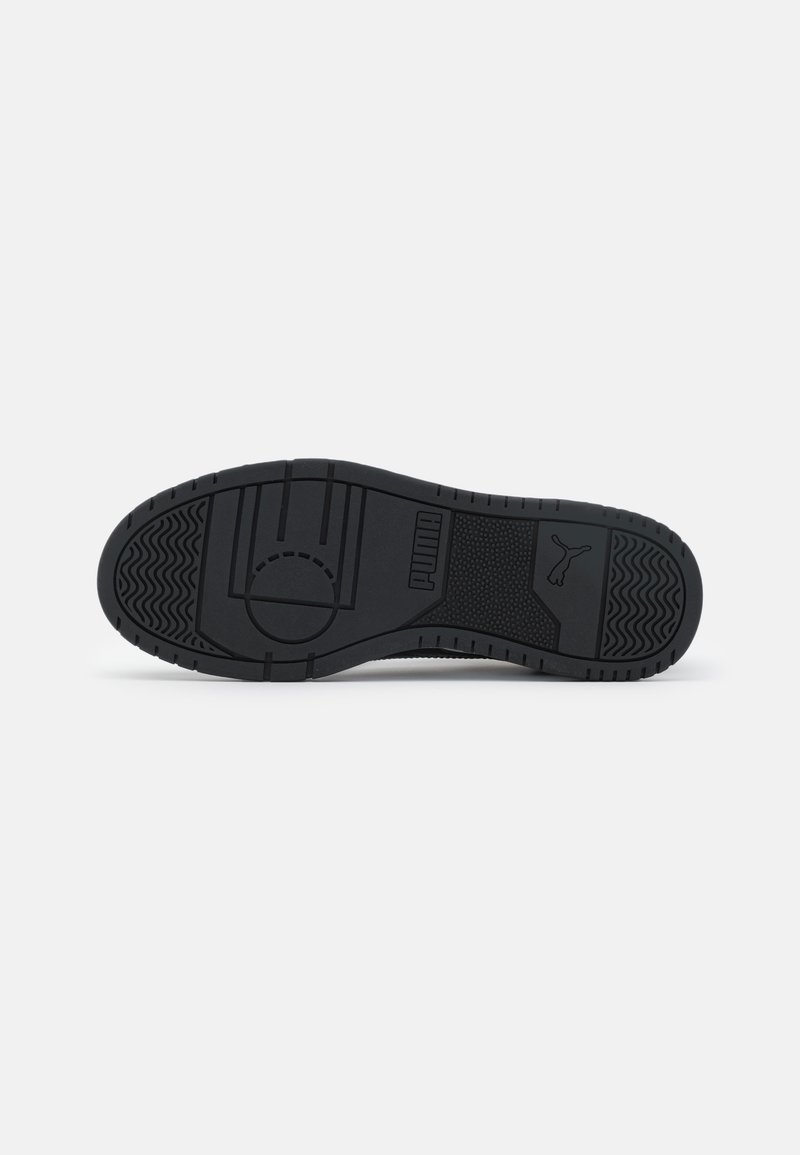 Semelle de sneaker en caoutchouc noir avec des motifs texturés, un design central en cercle et une marque proéminente en lettres en relief.