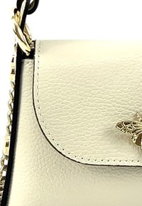 Sac à main en cuir crème avec une finition texturée, bandoulière en chaîne dorée et un accent décoratif en forme d'abeille dorée sur le rabat.