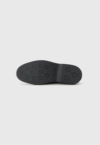 Zwarte rubberen schoenzool met een cirkelvormig textuurpatroon voor grip, rechthoekige vorm en geperste branding. Gladde afwerking met een uniforme kleur.