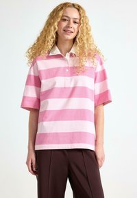 Polo a maniche corte a righe rosa e rosa chiaro con colletto bianco e patta con tre bottoni. Tessuto di trama liscia, vestibilità rilassata.