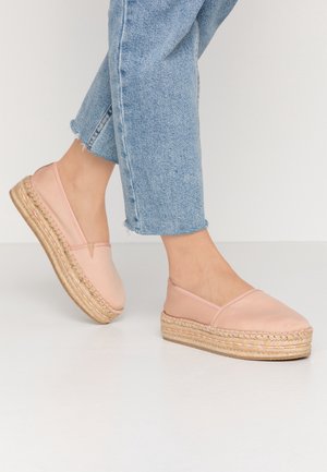 Personne portant des chaussures espadrilles à plateforme rose clair avec des semelles en corde tressée et un jean bleu clair raccourci.