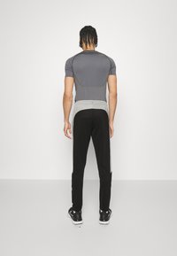 Kurze graue Sport T-Shirt mit Panellayout, kombiniert mit schwarzen Hosen mit grauen Akzenten und einem Kordelzugbund.