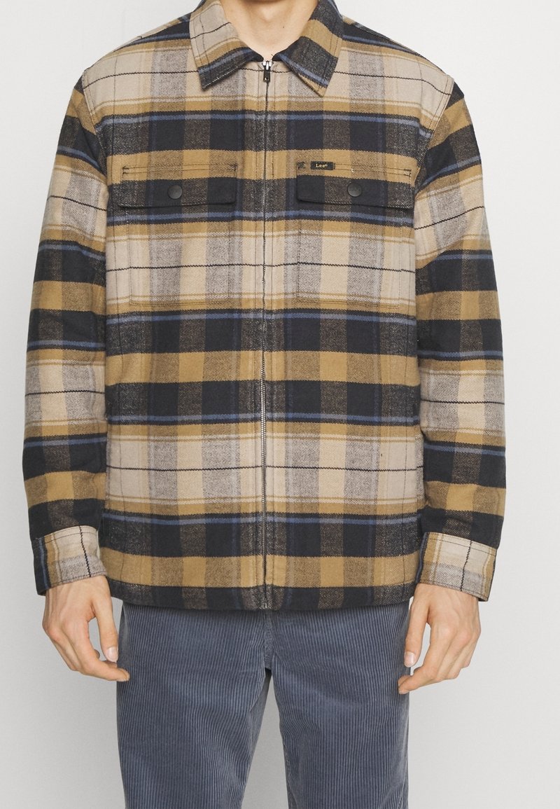 Hnědá, béžová a námořnická kostkovaná flanelová bunda se zapínáním na zip, dvěma předními kapsami na cvočky a límečkem.