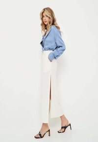 Bluză din satin bleu deschis, fustă albă cu slit înalt și sandale negre cu toc și curele. Texturi netede, siluetă ajustată și design modern.