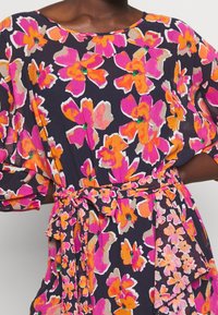 Vestido floral con vibrantes flores en tonos rosa, naranja y púrpura sobre un fondo marino. Tejido ligero con cintura ceñida y dobladillo con volantes.