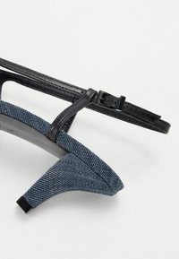 Μαύρη γόβα με τακούνι και τζιν λεπτομέρεια. Διαθέτει υφή από μπλέ ύφασμα στην περιοχή των δακτύλων και μια κομψή μαύρη λωρίδα με λεπτομέρεια από πόρπη.