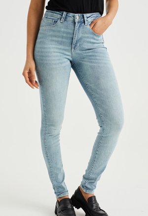 Vaqueros skinny de tiro alto en azul claro, fabricados en denim; presentan bolsillos frontales, cierre de botón y una textura suave.