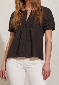 Blusa nera a maniche corte con scollatura a chiave, tessuto texturizzato e cuciture decorative. Abbinata a jeans chiari.