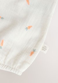 Tissu blanc doux avec de petits motifs de carottes orange et une étiquette cousue indiquant "little one" près du poignet élastique.