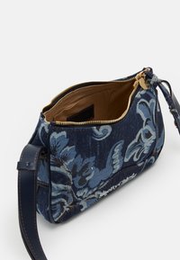 Borsa a tracolla in denim con motivi floreali blu, zip dorata e interno marrone. Include una tracolla in pelle removibile.