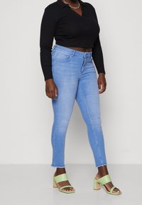 Ljusblå skinny jeans med fransar i kanten, ihopparade med en svart långärmad topp och gröna klacksandaler med breda remmar.