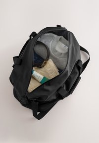 Must kott läbipaistva topiga, sisaldades halli pusa, rätikut, kehakreemi ja vööd. Omab kahte tõmblukku ja kangast rihmasid.