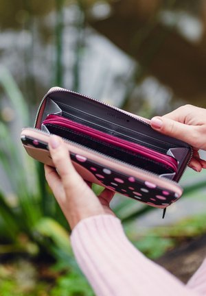 Zippered wallet featuring a black exterior with pink polka dots. Opens to reveal multiple compartments in gray and dark red fabric.