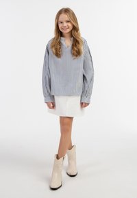 Stribet blå og hvid bluse med lange ærmer, parret med en hvid denimnederdel og beige cowboy støvler. Glat stoftekstur hele vejen igennem.