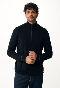 Pullover nero con mezza zip realizzato in tessuto morbido, caratterizzato da maniche lunghe, polsini a costine e una texture liscia. Indossato sopra pantaloni in denim.