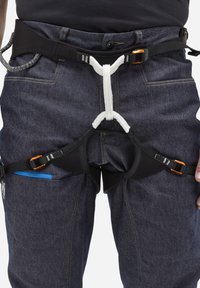 Czarna uprząż wspinaczkowa z pomarańczowymi elementami, regulowanymi paskami i białymi oraz szarymi detalami w postaci liny, noszona na ciemnych dżinsach z niebieskimi akcentami.