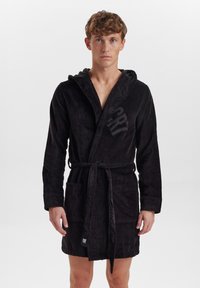 Black hooded bathrobe made of soft, textured fabric. Features a tie belt, two front pockets, and a logo on the chest.