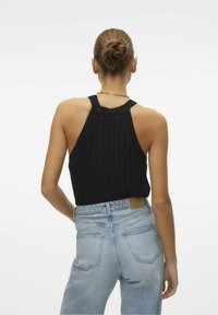 Czarny, prążkowany top na ramiączkach z szerokimi ramiączkami, zestawiony z jasnoniebieskimi, wysokimi dżinsami. Ciekawe detale to teksturowany materiał i dżinsowy krój.