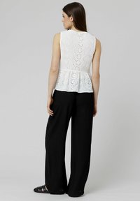 Haut peplum blanc avec détails en œillets, manches courtes et col rond, associé à un pantalon noir à larges jambes. Design simple et aéré.