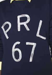 Navy blue sweatshirt with a textured white graphic reading "PRL 67." Features a yellow collar and standard crew neck design.