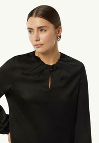 Schwarze Satinbluse mit gerafftem Ausschnitt, Schlüsselhole-Detail und langen Ärmeln mit elastischen Bündchen. Glatte Textur mit lässiger Passform.