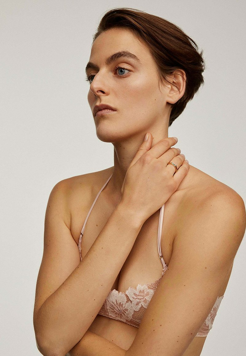 Sujetador de encaje en rosa suave con patrón floral, tirantes finos ajustables y un delicado acabado en los bordes. Textura suave.