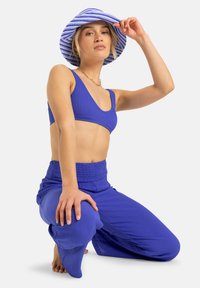 Conjunto de dos piezas en un vibrante tejido acanalado azul, que incluye un top corto y pantalones sueltos con cintura elástica, acompañados de un sombrero tipo cubo a rayas.