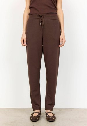 Braune Jogginghosen aus weichem Stoff, mit einem Kordelzugbund, schmal zulaufenden Beinen und seitlichen Taschen. Strukturiert braune Ballerinas runden den Look ab.