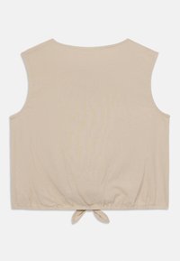 Beige ermeløs topp med rund hals og innsnøring i bunnen. Har en bundet detalj i hemmet og er laget av mykt, lett stoff.