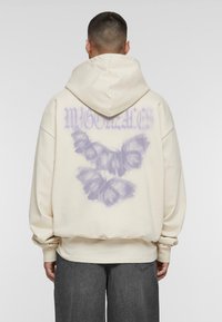 Creme hoodie med et stort, lilla sommerfuglegrafik på ryggen, der har en afslappet pasform og rummelig hætte. Fremstillet af blødt stof.