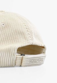 Gorra de pana crema con canalones verticales, un logo bordado en la parte posterior y una correa ajustable con una hebilla de metal.