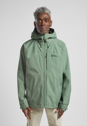 Veste verte résistante à l'eau avec capuche, comprenant un zip frontal, des poignets élastiques et un logo sur la poitrine. Texture lisse, design léger.