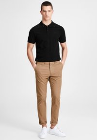 Polo noir, chinos beige et baskets blanches. Design simple avec des manches courtes et un col à trois boutons pour la chemise.