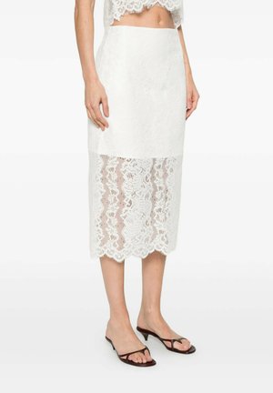 Donna che indossa una gonna midi in pizzo bianco con un pannello superiore solido e pizzo floreale trasparente nella parte inferiore, abbinata a sandali neri con tacco kitten.