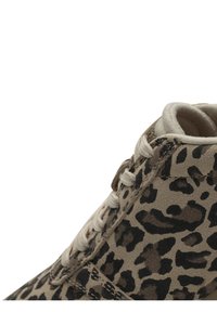 Gros plan sur une basket beige avec des imprimés léopard marron foncé et noir ainsi que des lacets blancs, montrant le col de la cheville et les détails de couture.