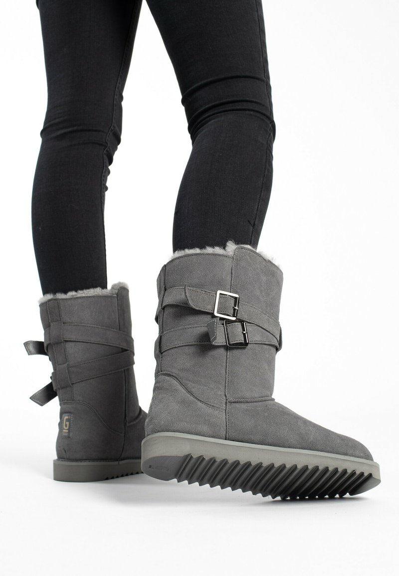 Botas de ante gris con un forro de piel suave, que cuentan con dos correas ajustables y una suela de goma texturizada con surcos.