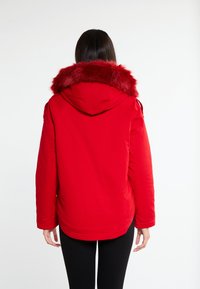 Rode winterparka met een nepbont capuchon, voorzien van een gladde textuur en een licht gebogen zoom aan de achterkant.